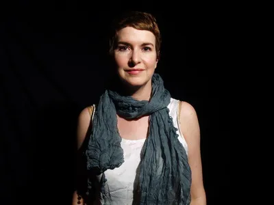 Viviane in a green scarf and white shirt against a black background