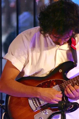 Matthew playing a sunburst guitar looking down in a white button shirt